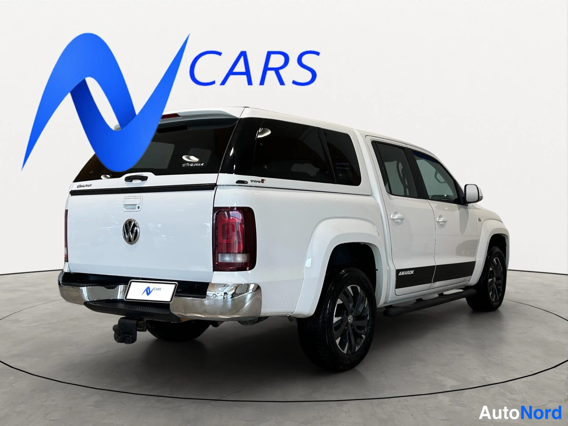 Takaviisto: Valkoinen Volkswagen Amarok -nappakuorma-auto kolmasosan takakuvaan, perä vasemmalla.