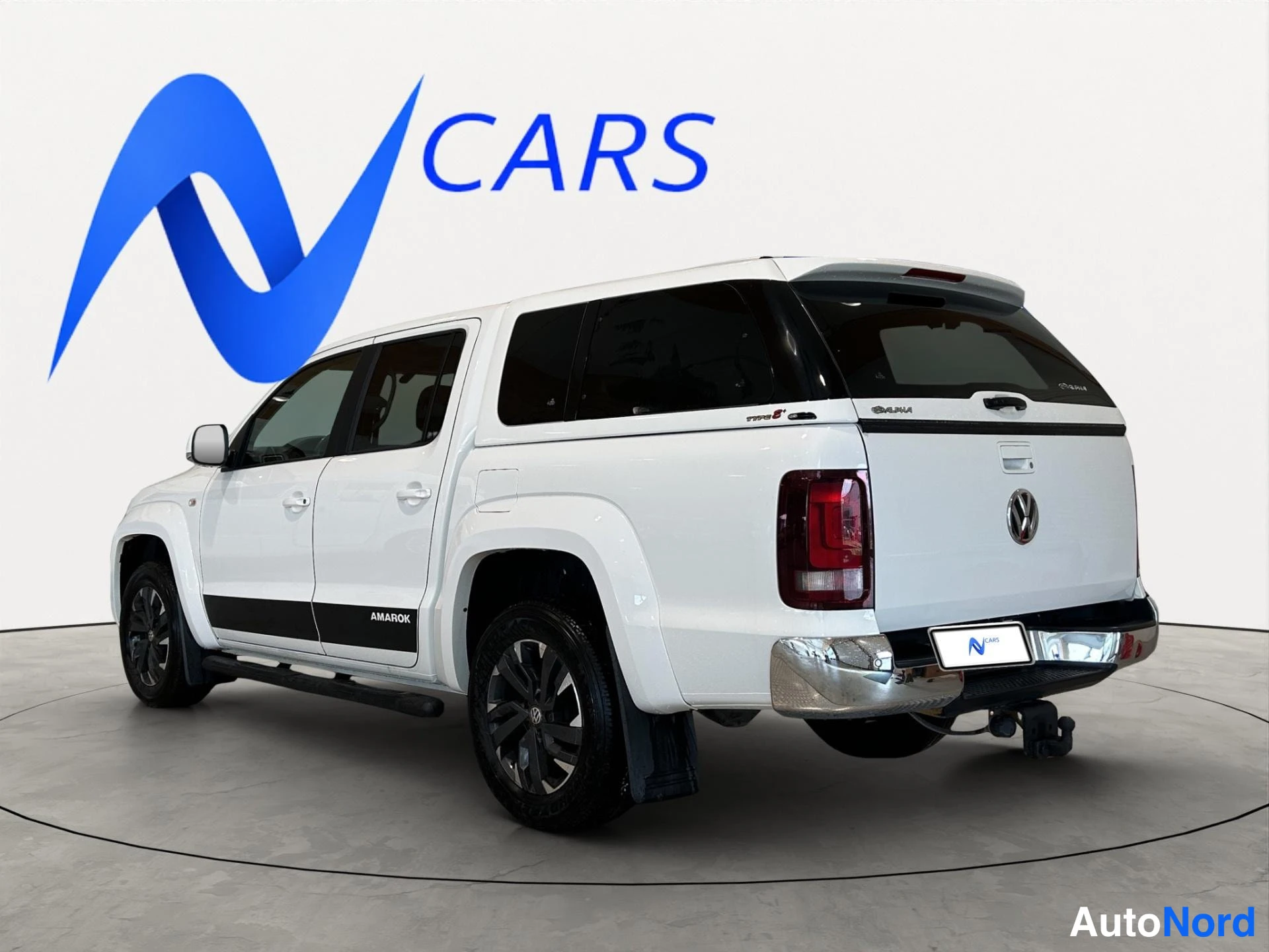 Takaviisto: Valkoinen Volkswagen Amarok -nappakuorma-auto kolmasosan takakuvaan, perä oikealla.