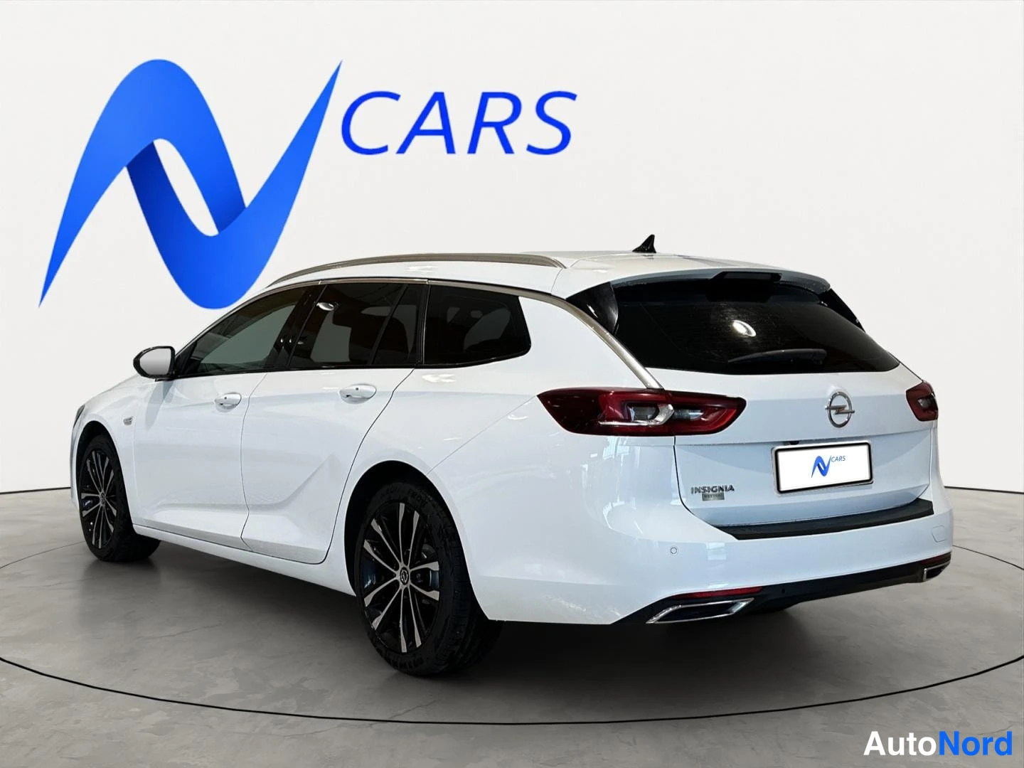 Takaviisto: Valkoinen farmariauto takaa kolmesta neljänneksestä, peräosa oikealla, Opel-merkki ja INSIGNIA-teksti peräluukussa.