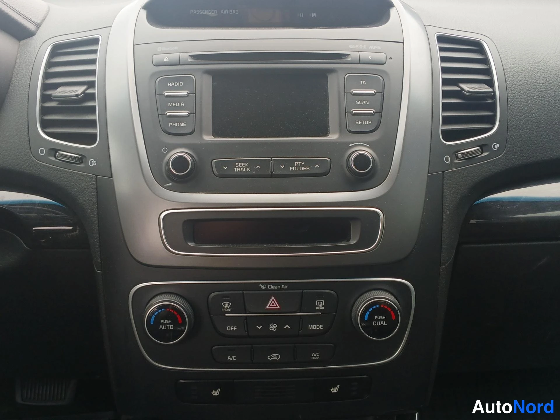 Takaa: Kia Sorenton keskikonsolin sisänäkymä: radiopaneeli (RADIO, MEDIA, PHONE, TA, SCAN, SETUP), Clean Air -kaksoisilmastointi (PUSH AUTO, PUSH DUAL, A/C), varoitusv
