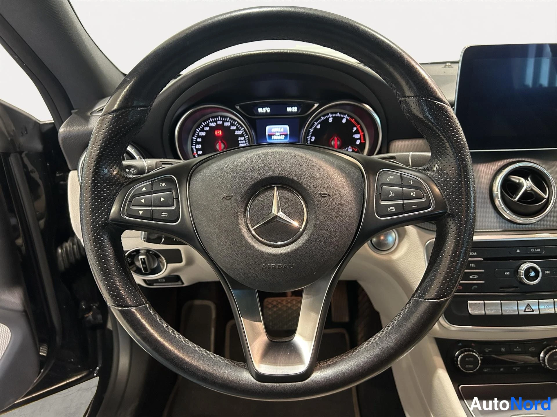 Yksityiskohta: Ohjaustilanne Mercedes-Benzissä: musta koristeltu ohjauspyörä, sana AIRBAG ja Mercedes-tähti keskellä, nappiryhmät molemmin puolin, väri- ja kierrosmittarit tau