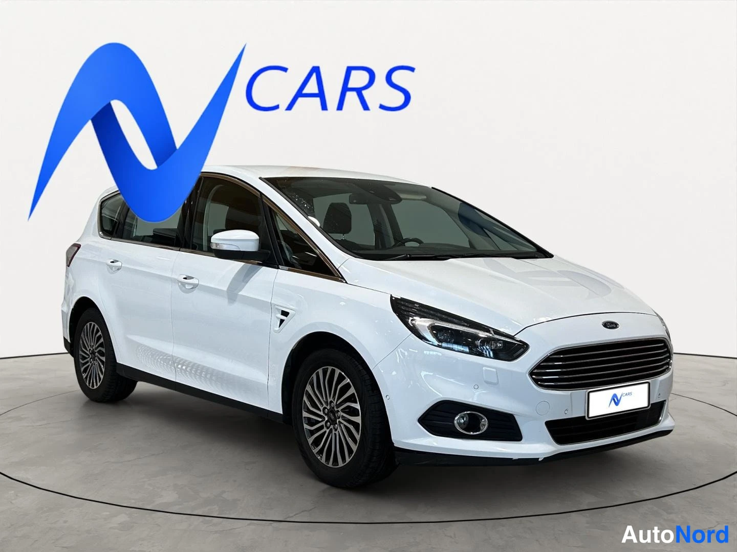 Etuviisto, nokka oikealle: Valkoinen Ford S-MAX -tilasmaasturi kulmassa edestä oikealta, koko auto näkyvissä studiotaustaa vasten.
