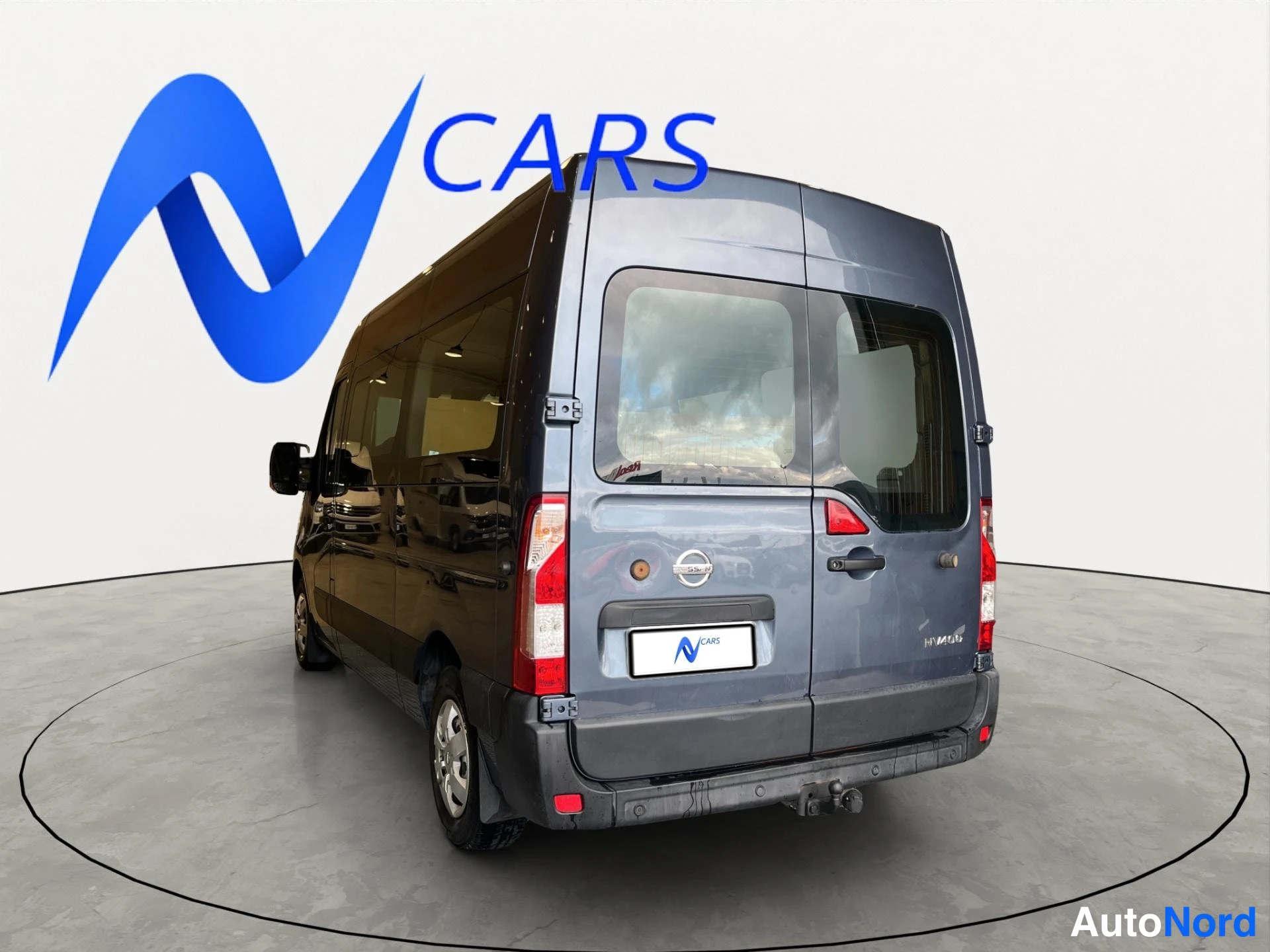 Takaviisto: Tummanharmaa Nissan NV400 -pakettiauto takaa kolmannelta suunnalta, peräosa ja vasen kylki näkyvissä; takaluukussa Nissan-merkki ja Ncars-kilpi.