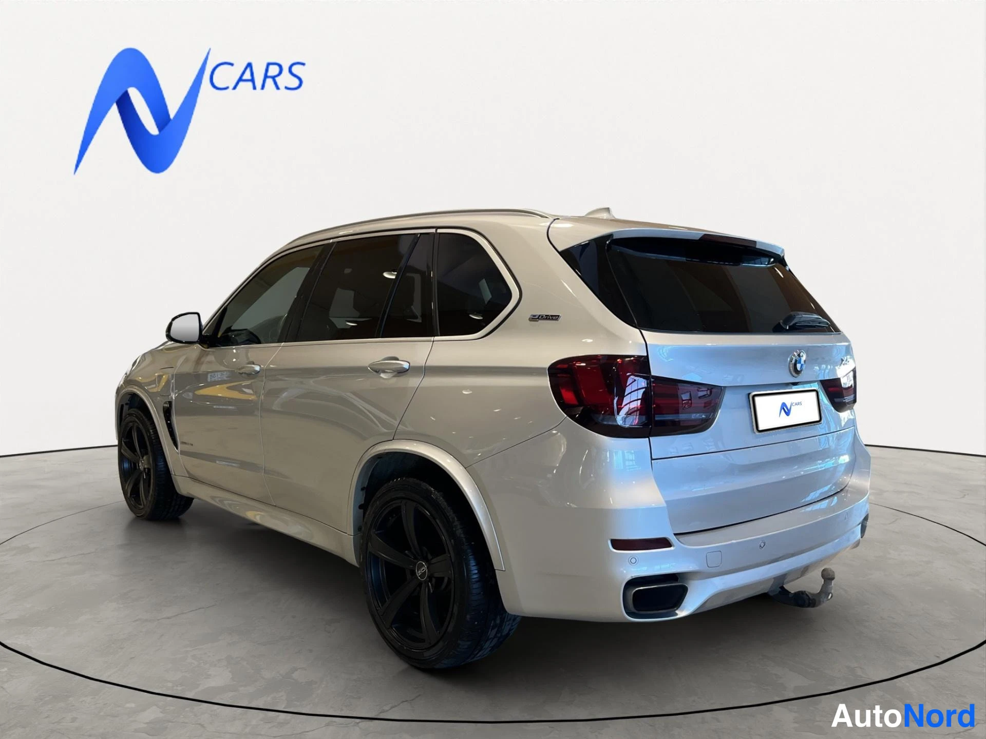 Takaviisto: Takakulmanäkyvä BMW X5, vaalea koriväri, mustat vanteet ja takana vetokoukku näkyvissä.