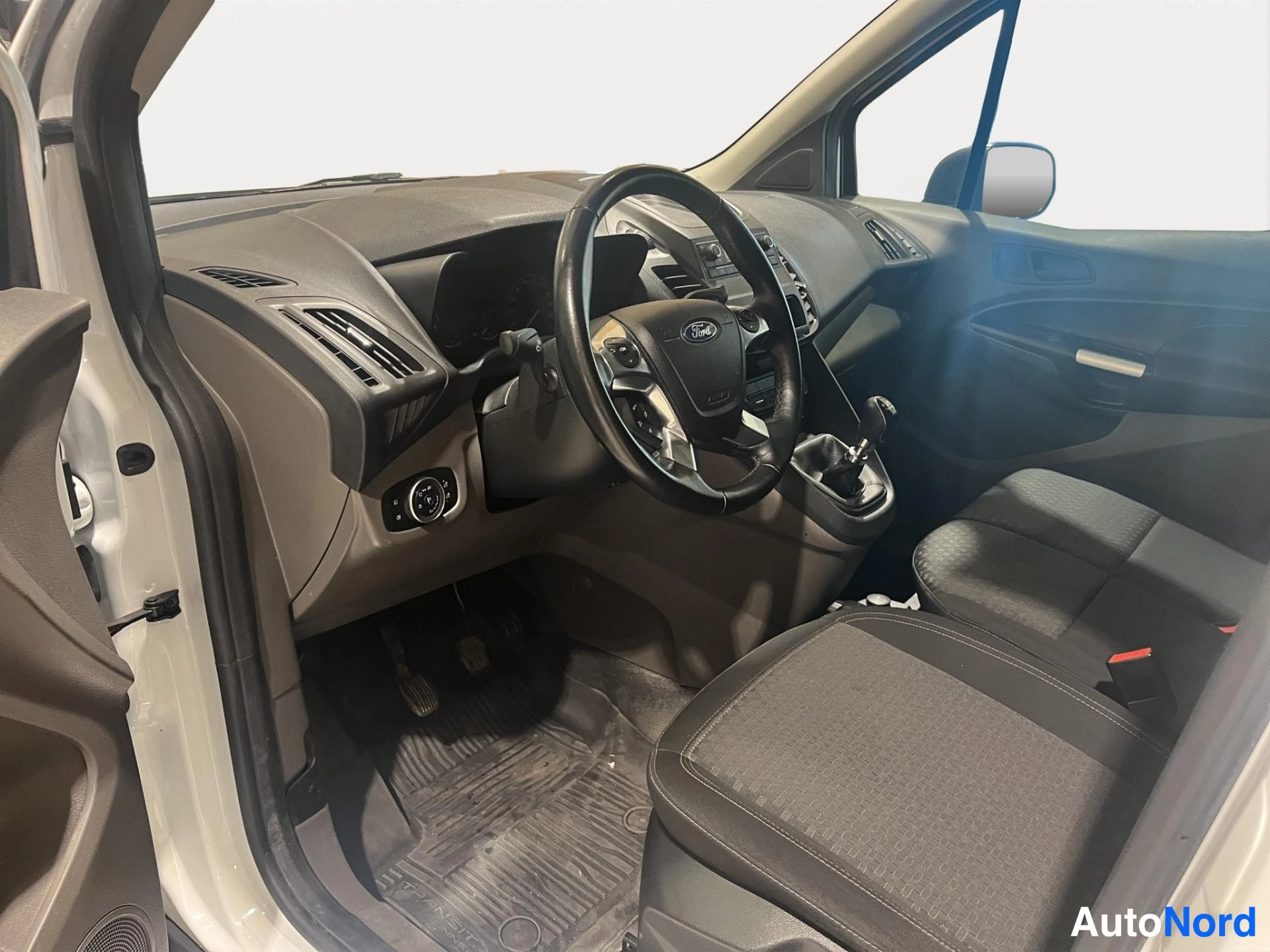 Muu: Ford Transit Connectin ohjaamo vasemmalta ovela katsottuna: ohjauspyörä, kojelauta, käsijarru, vaihdinsauva ja tummat istuimet.