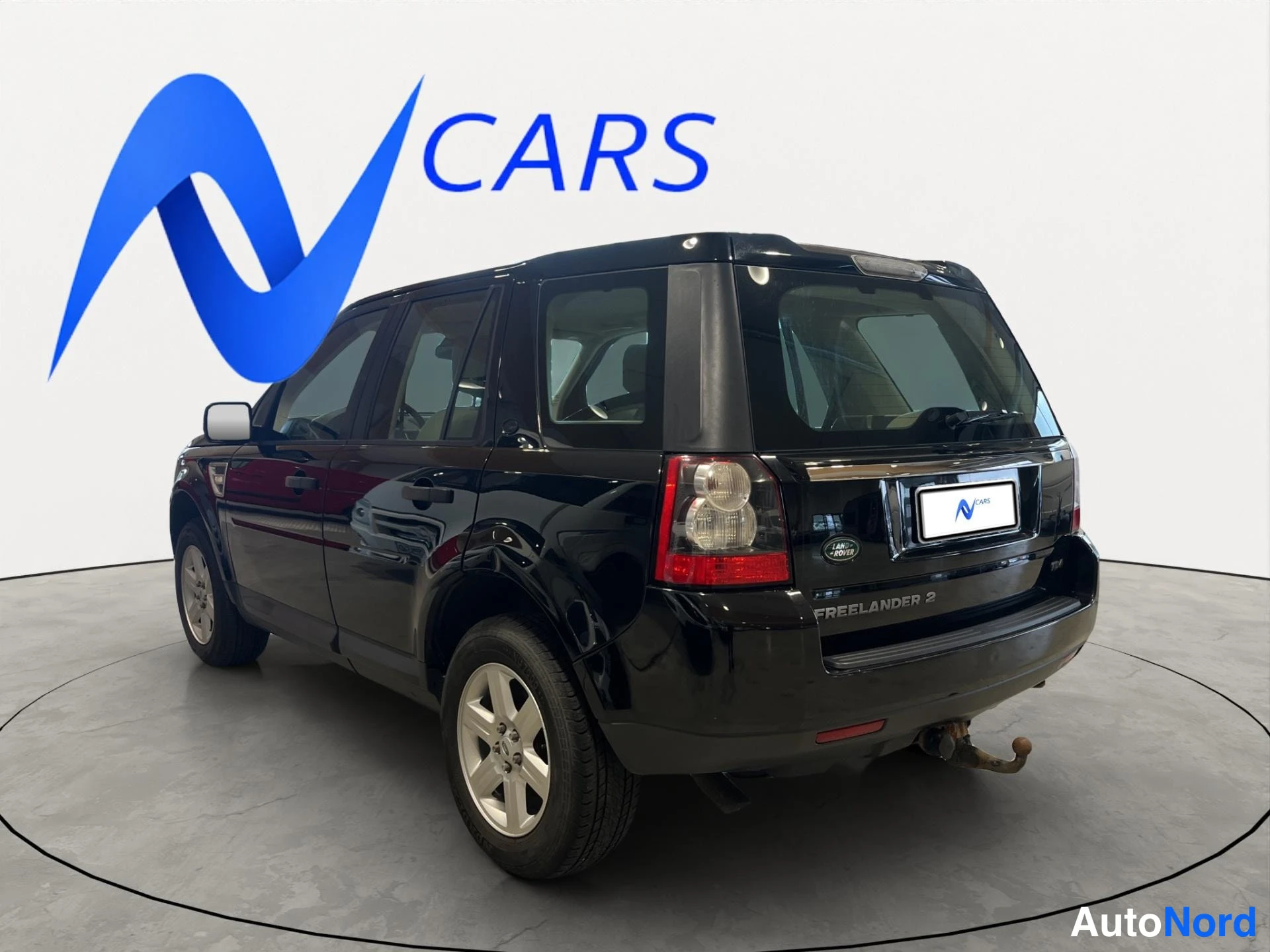 Takaviisto: Land Rover Freelander 2 takaosa sivulta takakulmasta, musta koripaintti, takaluukussa FREELANDER 2 -teksti ja Land Rover -merkki, vetokoukku näkyy.