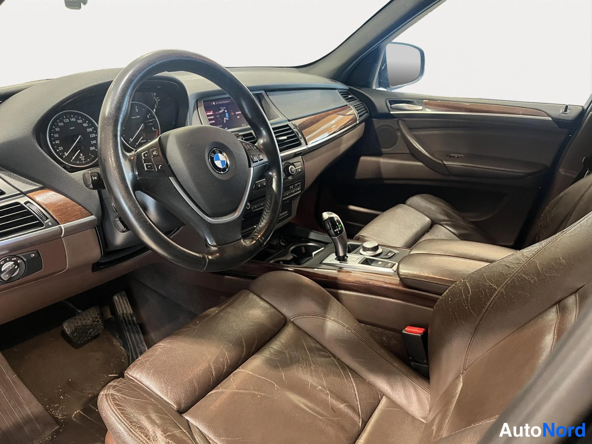 Muu: Ohjaamon kuljettajan puolen näkymä vasemmalta: BMW-ohjauspyörä, ruskeat nahkaistuimet ja puujanelia kojelaudassa.