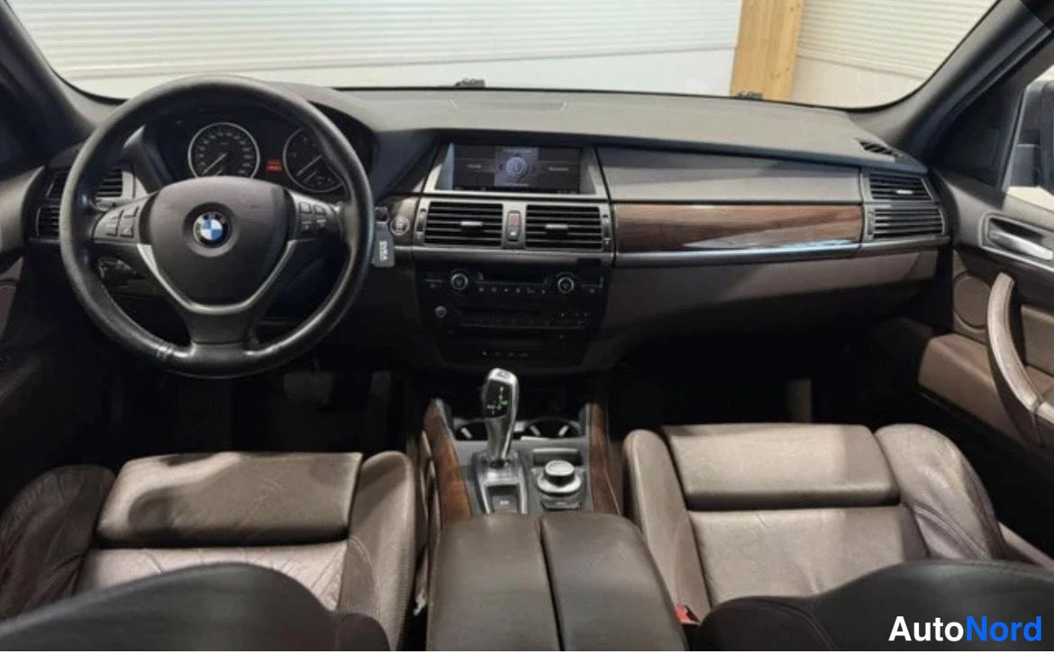 Edestä: auton ohjaamo:n kuljettajan näkymä BMW-ohjauspyörästä mittaristoon ja keskikonsolin infonäyttöön.