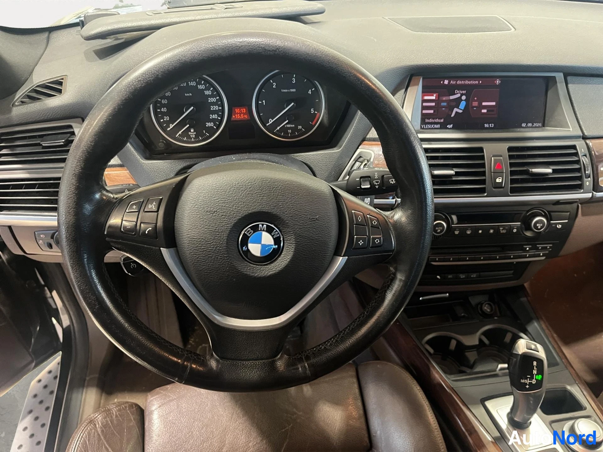 Yksityiskohta: BMW-merkkinen ohjauspyörä, mittaristo ja keskikonsoli, jossa näyttö ja vaihteenvalitsin.