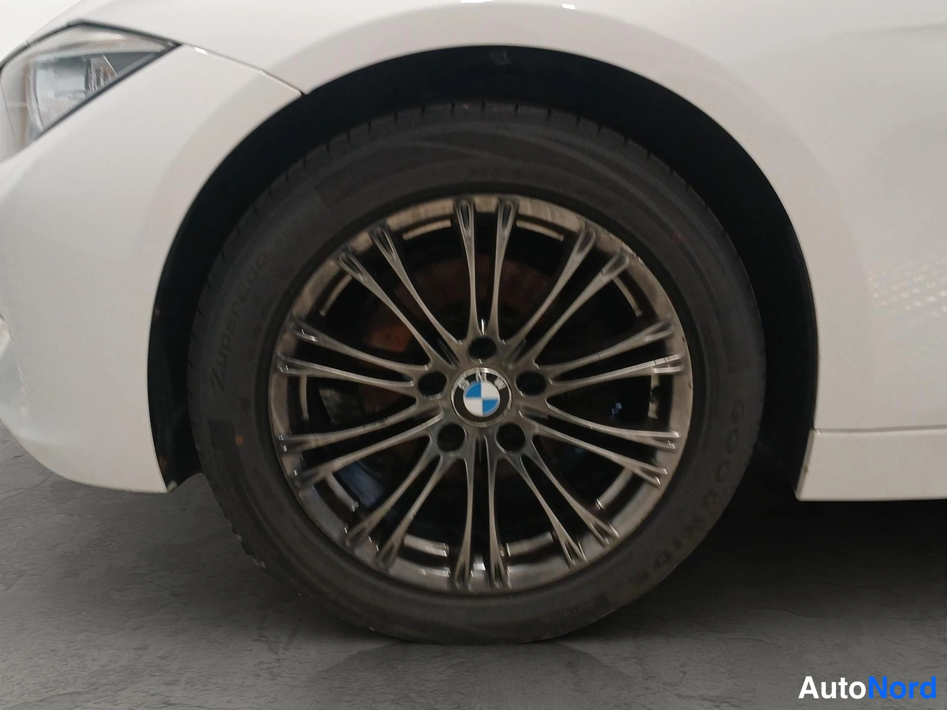 Muu: Valkoisen BMW:n etupyörä lähikuva, tumma monipuolammasvanna ja BMW-merkki nappikeskellä.