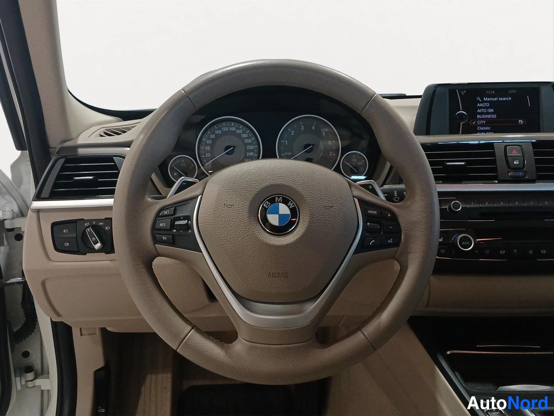 Sivulta: Ohjauspyörän ja kojelaudan näkymä kuljettajan näkökulmasta; ajotietokoneen näytöllä valikko ja BMW-merkki ohjauspyörässä.