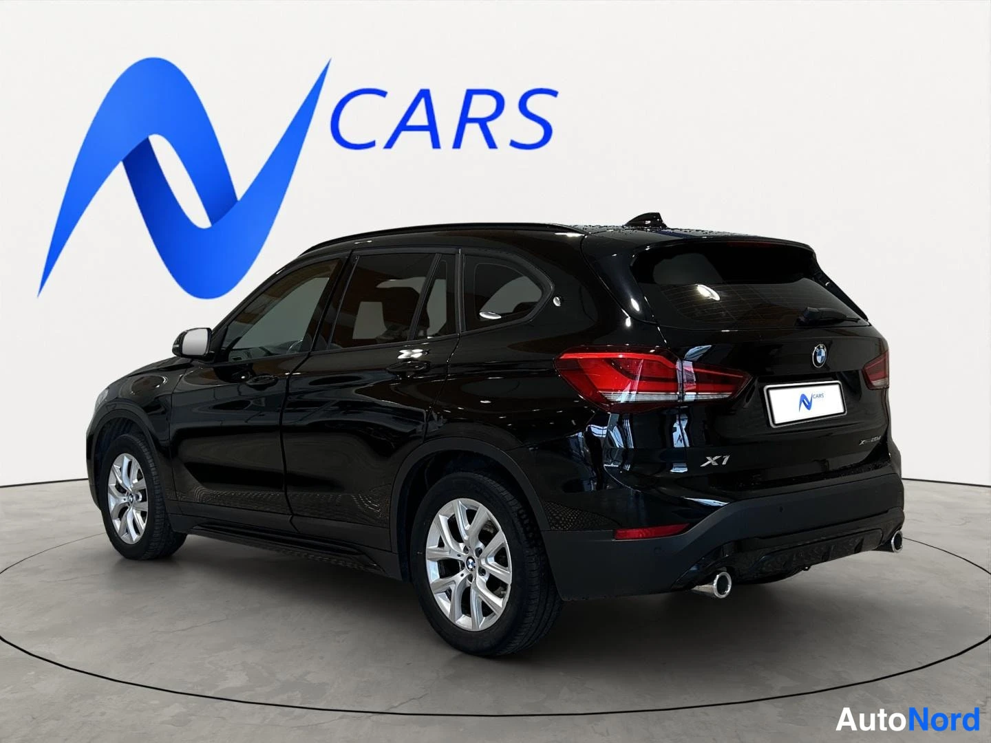 Takaviisto: Musta BMW X1 takakulmasta oikealta, takaovet, takavalot ja pakoputki näkyvät studiossa valkoista taustaa vasten.