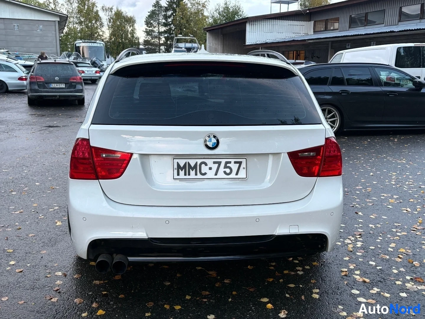 Takaa: Valkoisen farmariauton suora takakuva; rekisterikilpi, punaiset takavalot ja kaksi pakoputkea näkyvät.