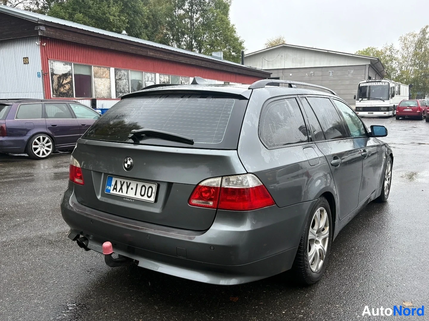 Takaviisto: BMW 5-sarjan farmari takaa viistosti oikealta kuvattuna, rekisterikilpi ja takakytkin näkyvät märällä pihalla.