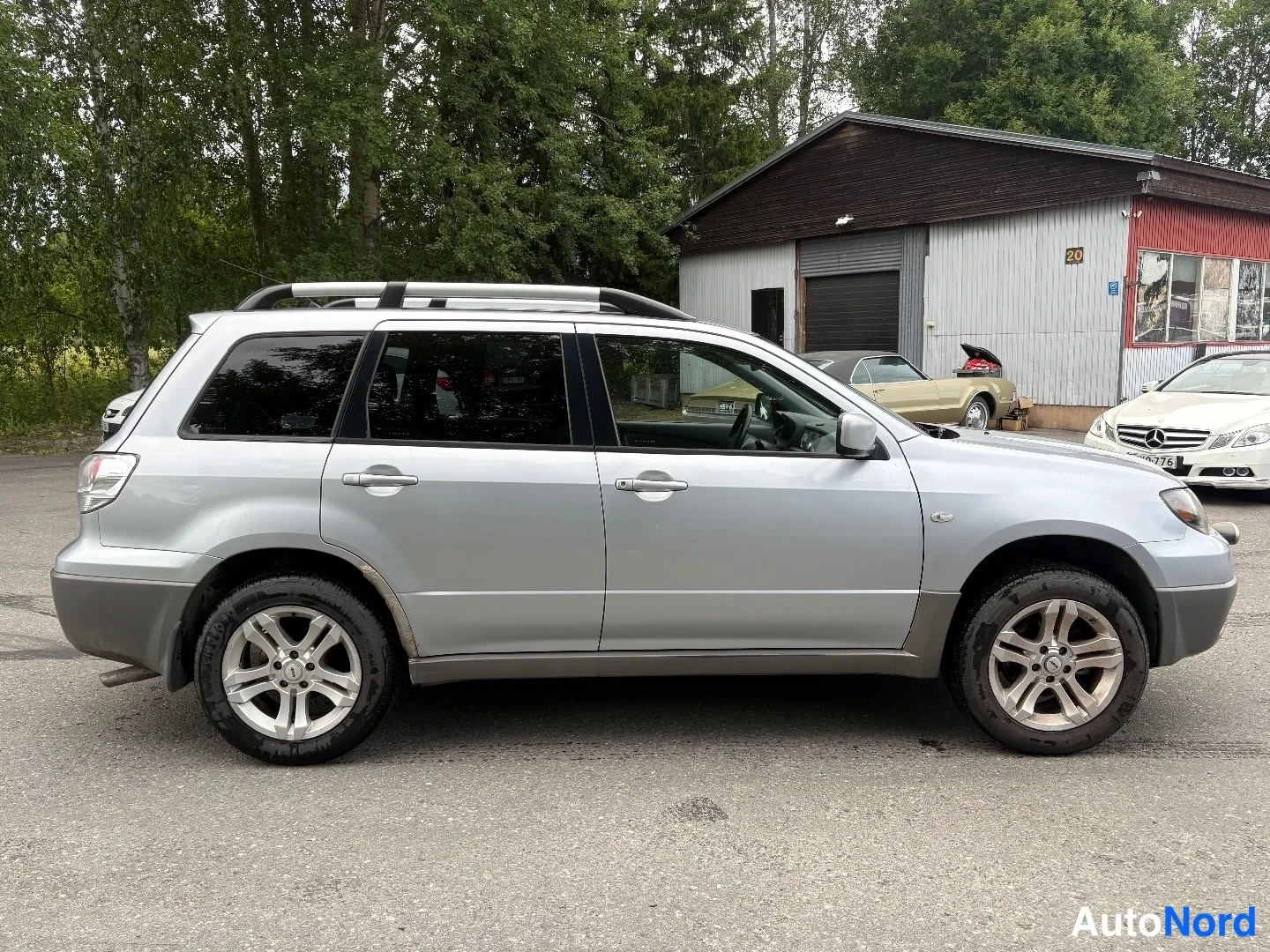 Etuviisto, nokka oikealle: Hopeanvärinen Mitsubishi Outlander sivulta oikeaan nurkkaan suunnattuna, kattokaiteet näkyvissä.