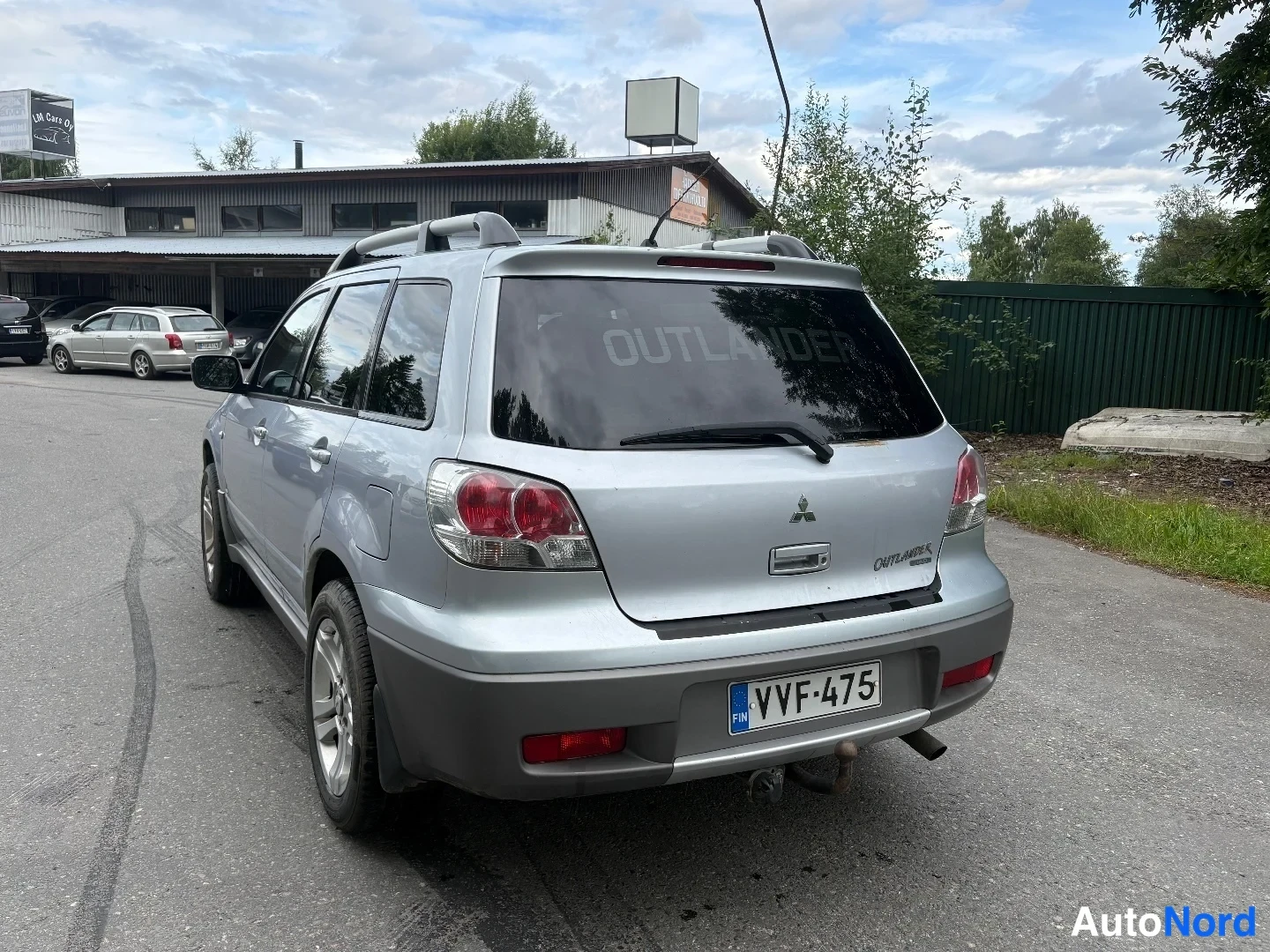 Takaviisto: Hopeanvärinen Mitsubishi Outlander takaa viistosti vasemmalta, takamoottori ja rekisterikilpi näkyvät.