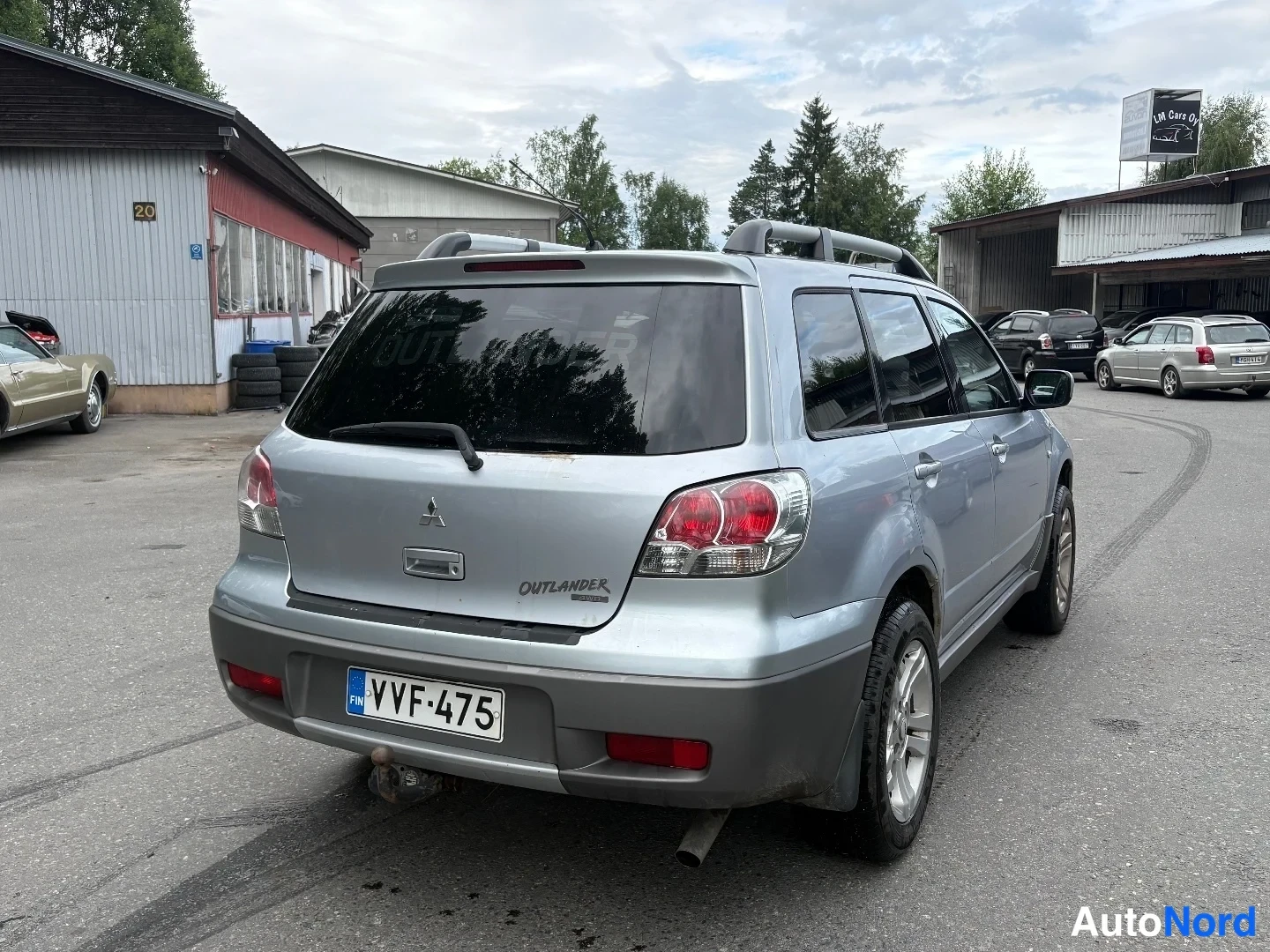 Takaviisto: Hopeanvärinen Mitsubishi Outlander takaa viistosti oikealta, rekisterikilpi ja kattokaiteet näkyvät.