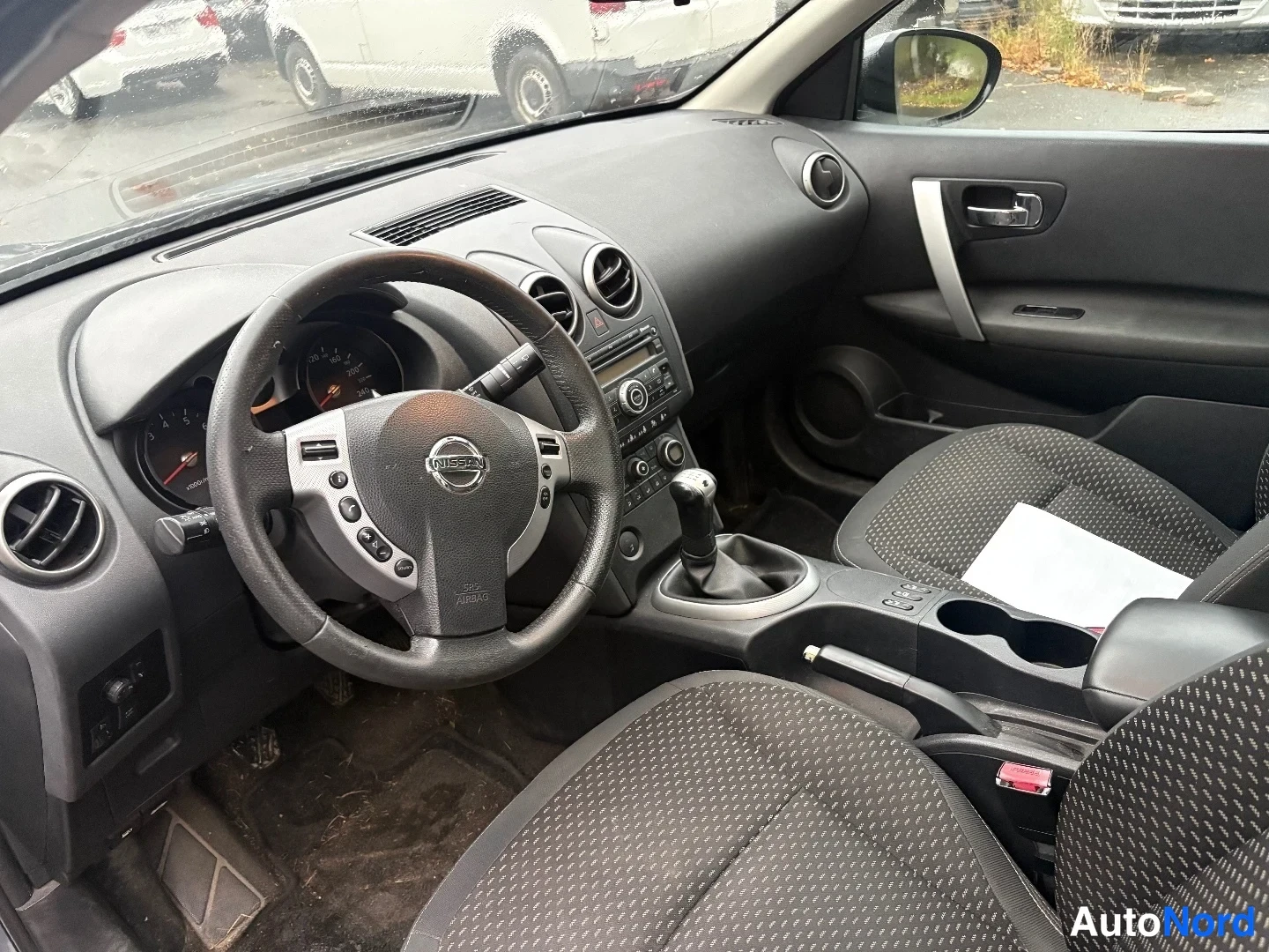 Muu: Ohjaamo kuvattuna kuljettajan oven suunnasta: Nissan-merkkinen ohjauspyörä, analogiset mittarit, manuaalivaihteisto ja kaksi etuistuinta kangasverhoilla.
