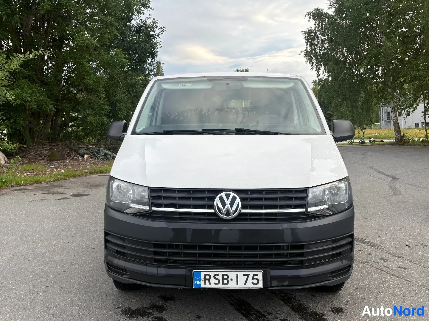 Edestä: Valkoisen Volkswagen Transporter -pakettiauton etunäkymä, musta etupuskuri, rekisterikilpi.