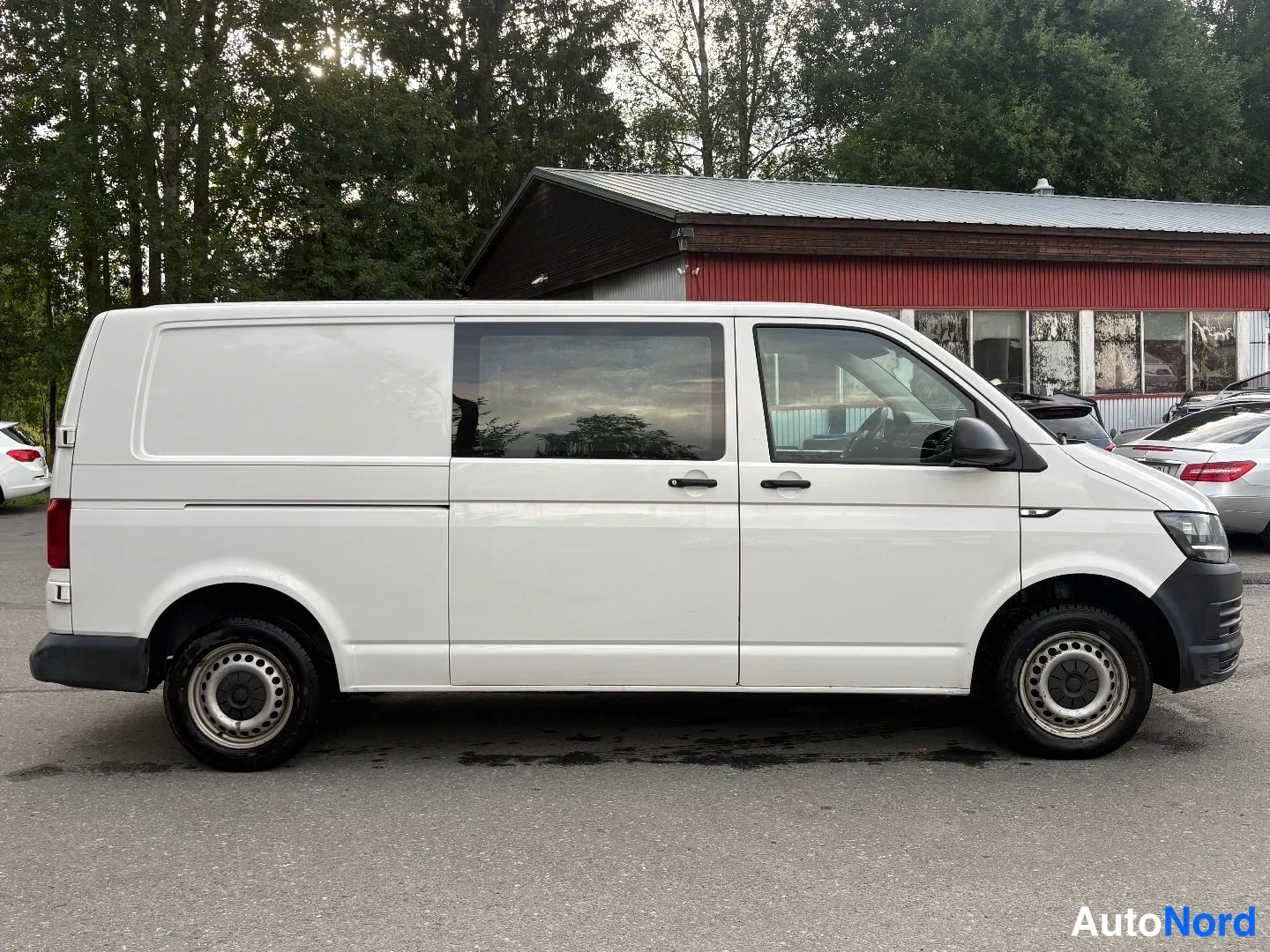 Sivulta: Valkoisen pakettiauton sivukuva vasemmalta puolelta; kolme ovea, tummat ikkunat ja teräsvanteet.