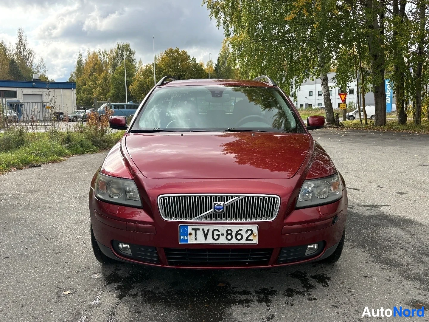 Edestä: Tummanpunaisen farmariauton suora etunäkymä, rekisteritunnus, Volvo-merkki konepellin etureunassa.