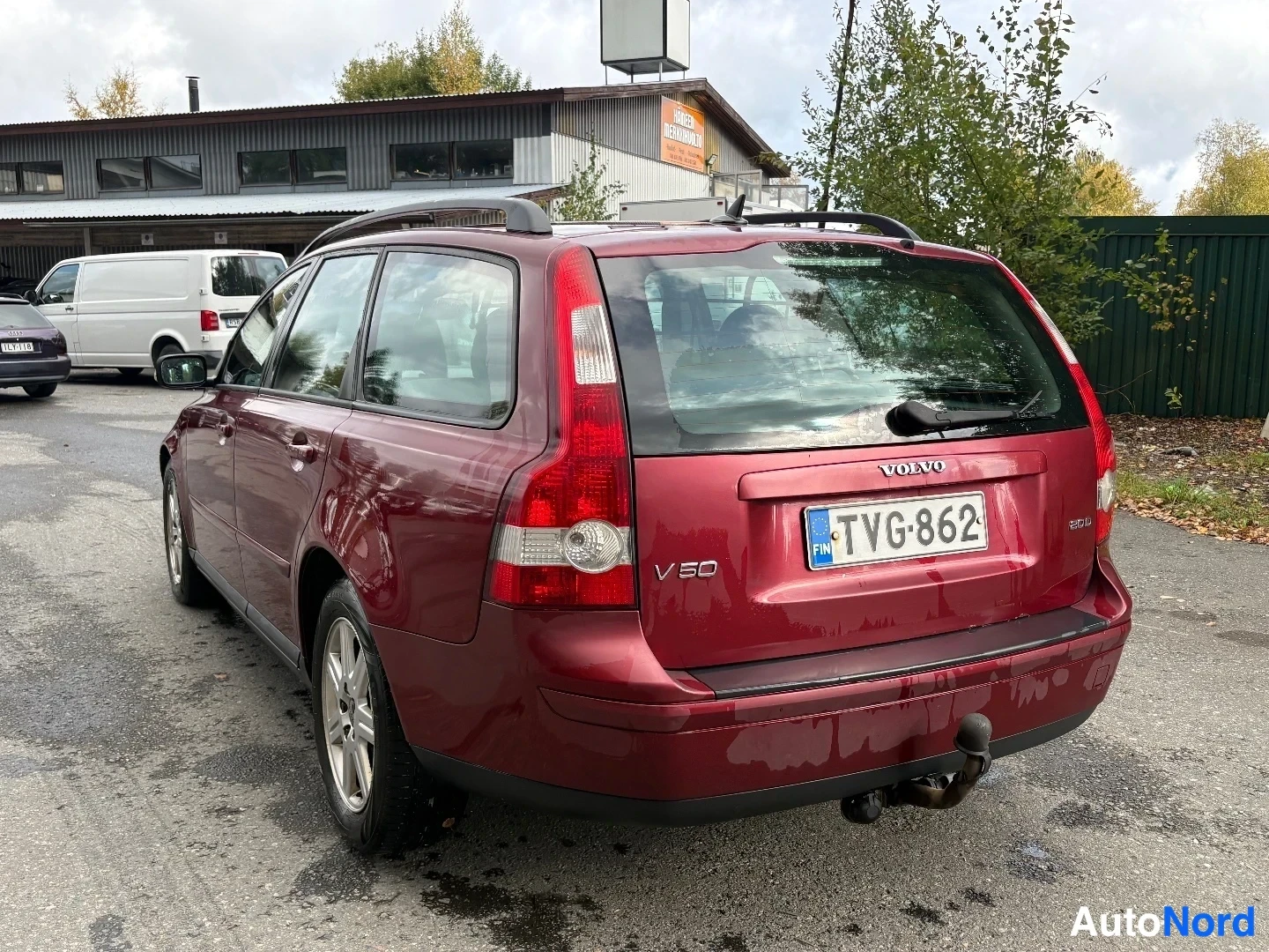 Takaviisto: Tummanpunaisen Volvo V50 -farmarin takaosa ja vasen kylki kolmaneljäkäs-kuvassa; rekisteritunnus, V50-merkintä ja Vetokoukku.