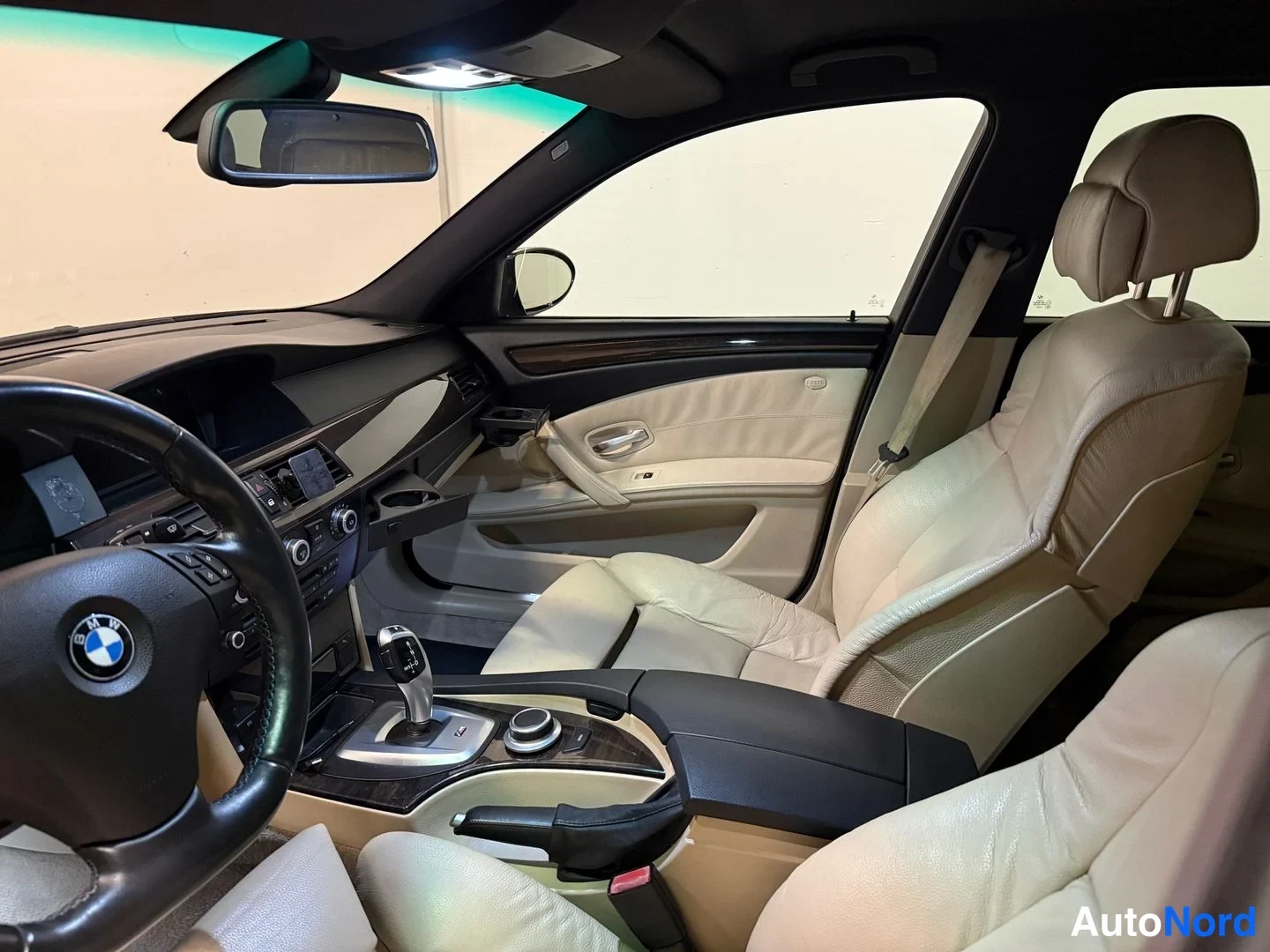 Edestä: Auton sisätilat: BMW-ohjauspyörä, automaattivaihteiston valitsin, iDrive-ohjain ja vaaleat nahkapenkit.