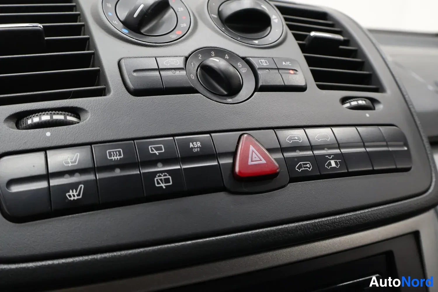 Yksityiskohta: Kojeiston nappirivi: ASR OFF, heater- ja mirror-lämmitysmerkit, istuinlämmitysmerkit, punainen varoituskolmio sekä avattavien ovien painikkeet.