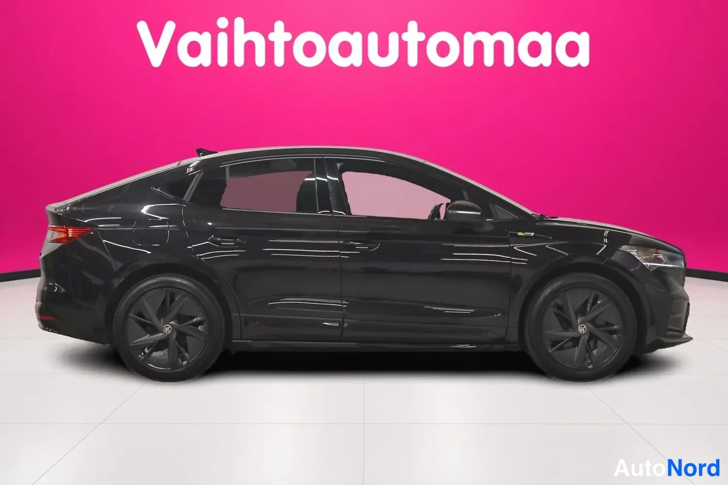 Etuviisto, nokka oikealle: Mustan Skoda Enyaq Coupé -auton kylki sivulta kuvattuna, keulan ajovalot ja takavalot sekä tummat alumiinivanteet näkyvät.