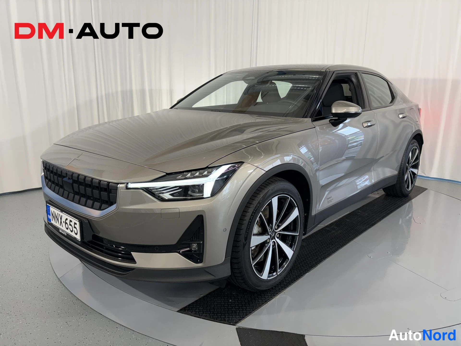 Etuviisto, nokka vasemmalle: Polestar 2 -sähköauto edessä vasemmalta kolmannesnäkymässä, hopeanbeige runko, rekisteri.