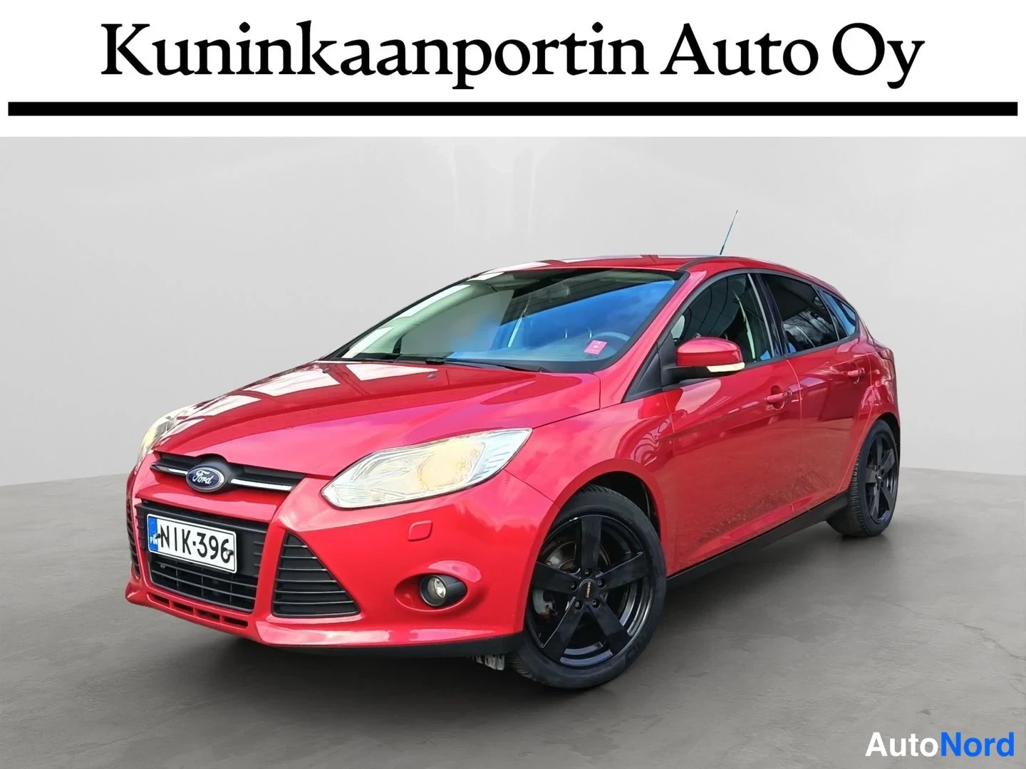 Etuviisto, nokka vasemmalle: Punainen Ford Focus -henkilöauto etuosa vasemmasta etukulmasta, rekisteritunnus, tummat vanteet.