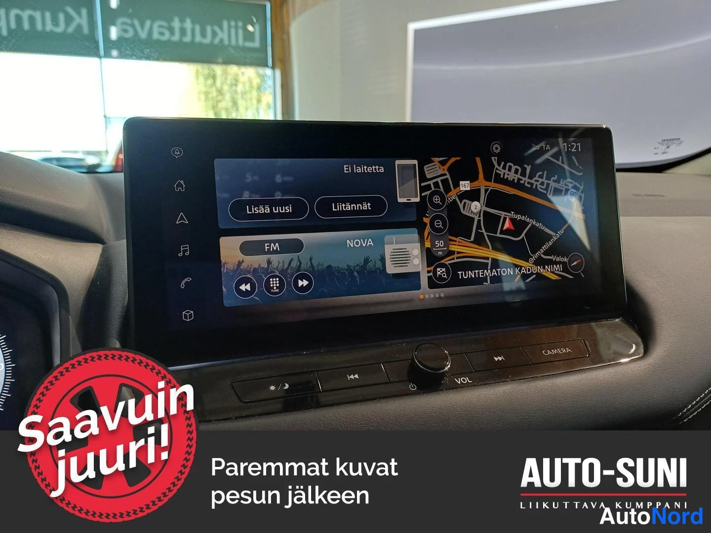 Yksityiskohta: Auton kojelaudan keskellä oleva kosketusnäyttö, jolla näkyy navigointikartta, FM-radio (NOVA) ja Bluetooth-kytkentäruutu teksteinä 'Lisää uusi' ja 'Liitännät'.