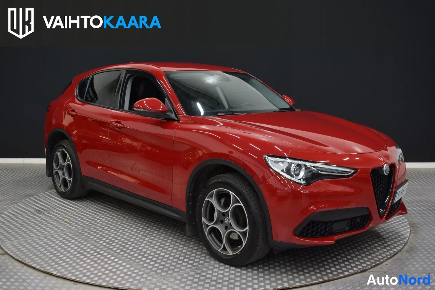Etuviisto, nokka oikealle: Punainen Alfa Romeo Stelvio etuviistestä oikealta kuvattuna, kilpi-ilmastointi ja pyöreät ajovalot näkyvät.