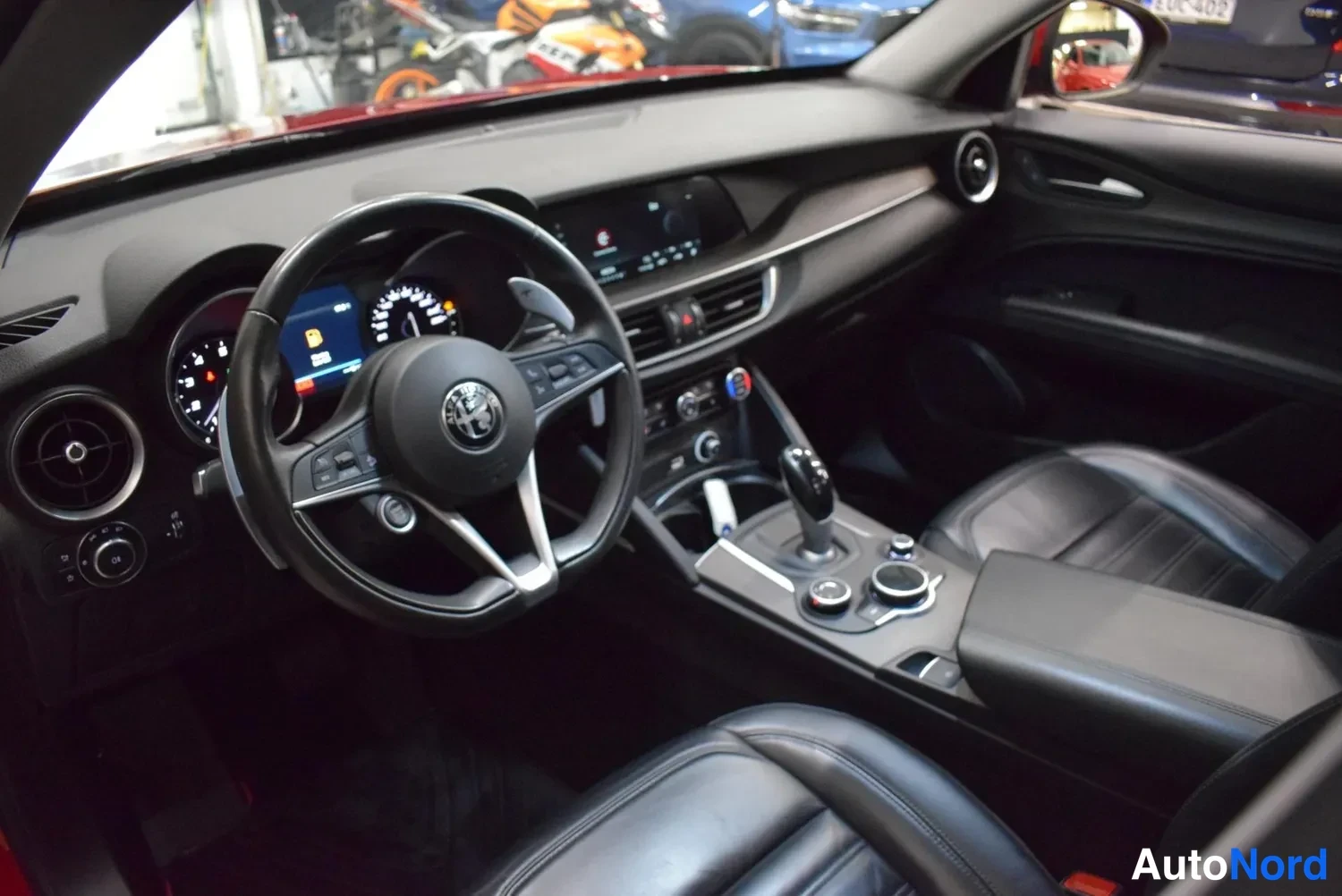 Muu: Ohjaamosta kuvattu näkymä: ratissa Alfa Romeo-logolla, digitaalinen mittaristo ja keskikonsolilla vaihtajanappi ja näyttö.
