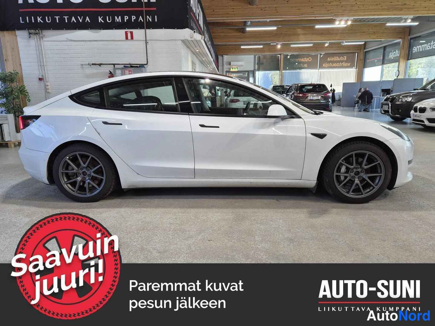 Sivulta: Valkoinen henkilöauto sivulta kuvattuna autonäyttelytilassa.