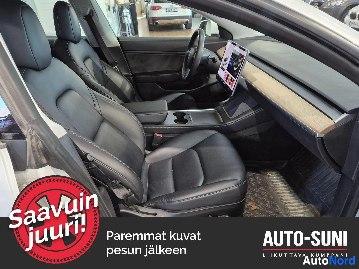 Muu: Tesla Model 3:n etumatkustustila: mustat istuimet, katsomossa puunvärinen kojelauta ja keskinäyttö.