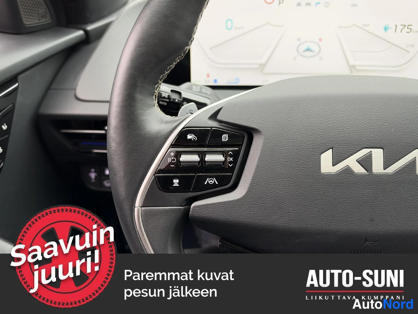 Edestä: Ohjauspyörän vasemman puolen näppäimet lähikuvassa: AUTO- ja ajoavustuspainikkeet sekä Kia-logon osa taustalla kojelautanäyttö.