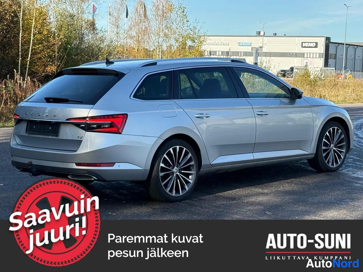 Takaviisto: Hopeanvärinen farmariauto takaa oikealta kuvattuna, perä ja kylki näkyvät, taustalla rakennuksia ja puita.