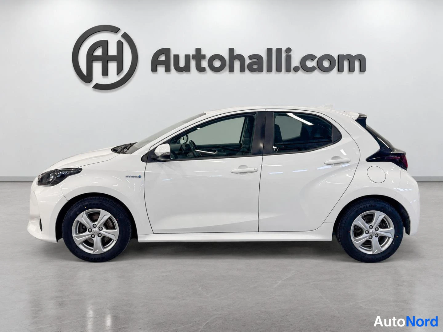 Sivulta: Valkoinen Toyota Yaris sivulta vasemmalta, HYBRID-teksti etulokasuojassa