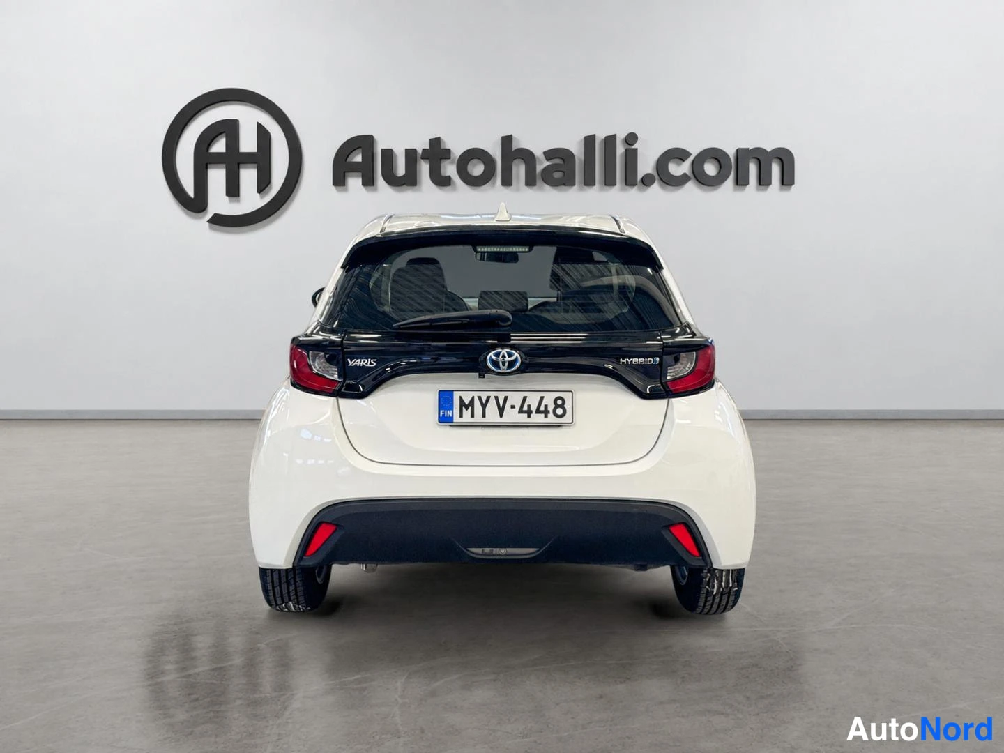 Takaa: Valkoinen Toyota Yaris suoraan takaa, rekisteritunnus, HYBRID-teksti takavalossa.