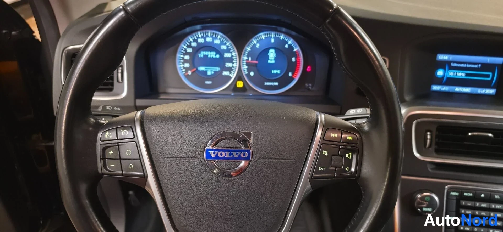 Muu: Volvo-merkillinen ohjauspyörä ja sen takana kojelaudan mittaristo, keskellä merkinanto ja 'VOLVO'-teksti.