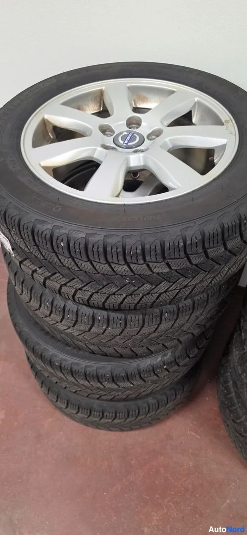 Yksityiskohta: Pino talvirenkaita; päällimmäisessä hopeinen alumiinivanne Volvo-merkillä.