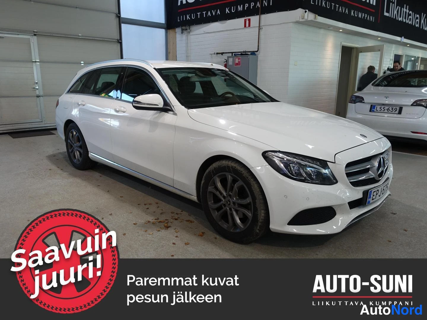 Etuviisto, nokka oikealle: Valkoinen Mercedes-Benz C-farmari kulmassa etuosa ja vasen kylki näkyvissä autosalissa, rekisteritunnus.