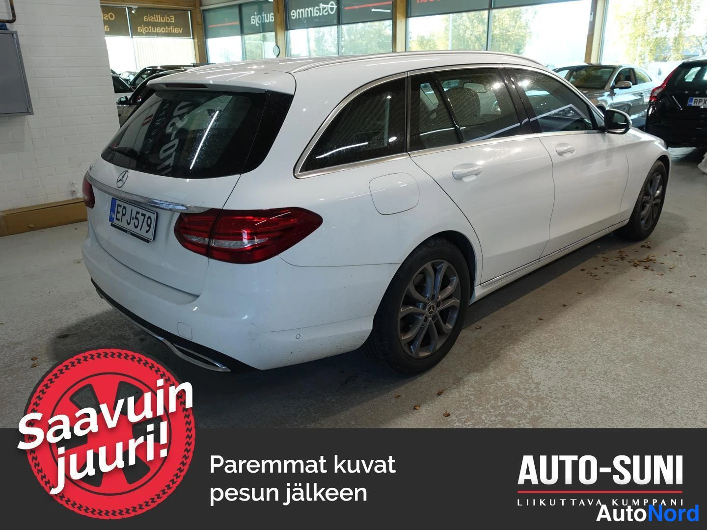 Takaviisto: Valkoinen Mercedes-Benz C-farmari takaosasta ja oikeasta kyljestä kulmassa kuvattuna autosalissa, rekisteritunnus.