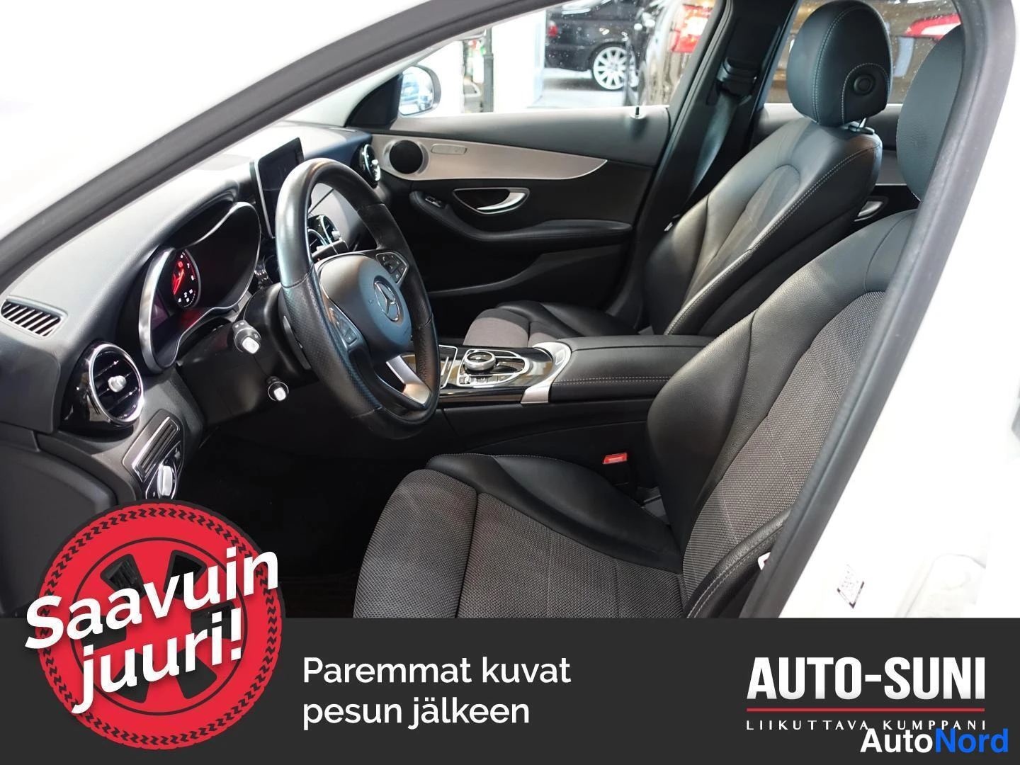 Edestä: Auton etupenkit ja ohjaamo vasemmalta kuvattuna; tummat istuimet, Mercedes-ohjauspyörä ja keskikonsoli näkyvät.