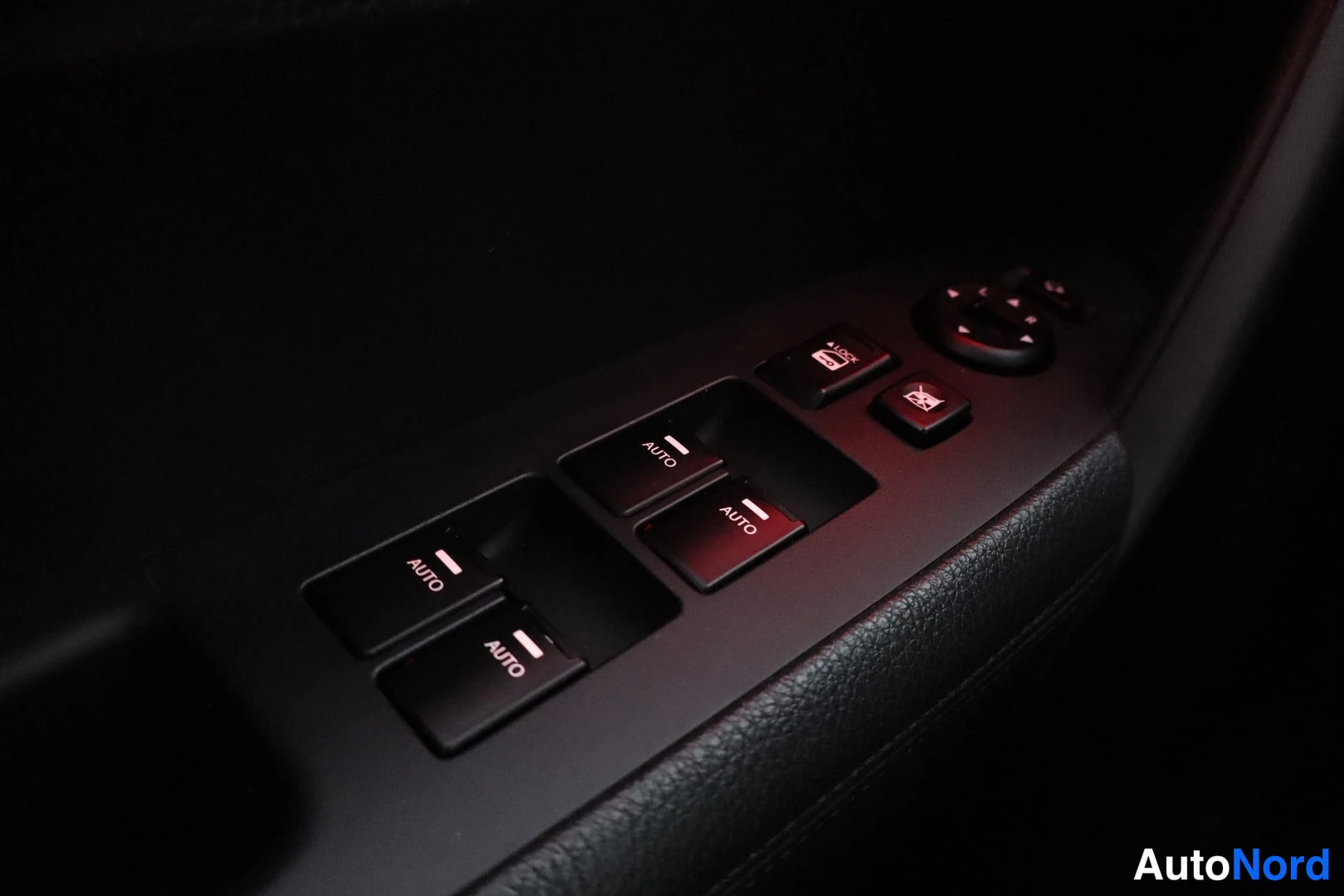 Yksityiskohta: Oven sähköikkunanostimen kytkinpainikkeet lähikuvassa, kaksi painikkeista AUTO-merkityillä, lisäksi peilisäädin ja lukituspainike.