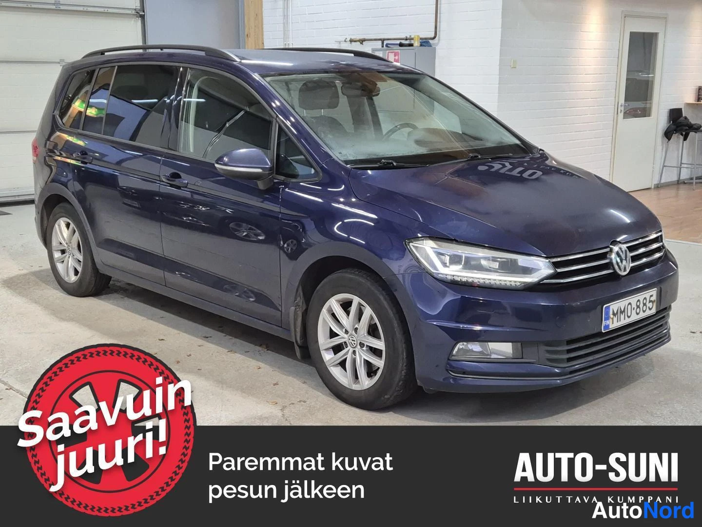 Etuviisto, nokka oikealle: Sininen Volkswagen Touran edessä oikealta vinosta, kokonaisuus näkyvissä sisätiloissa.