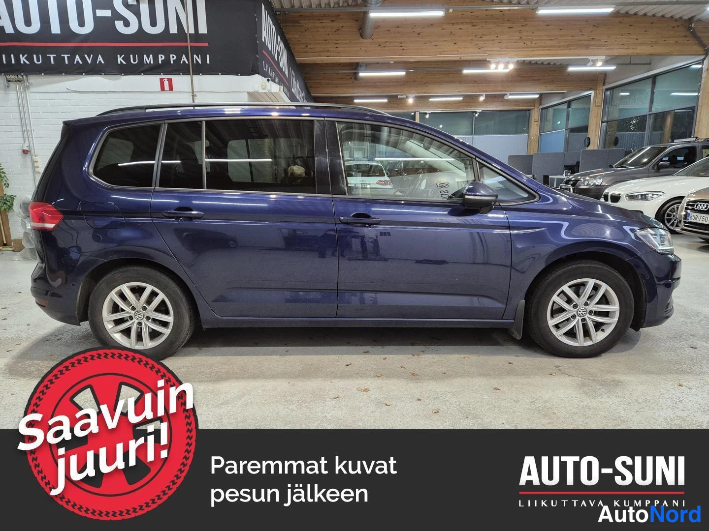 Sivulta: Sininen Volkswagen Touran kylki vasemmalta, kokonaisuus näkyvissä autosalissa.
