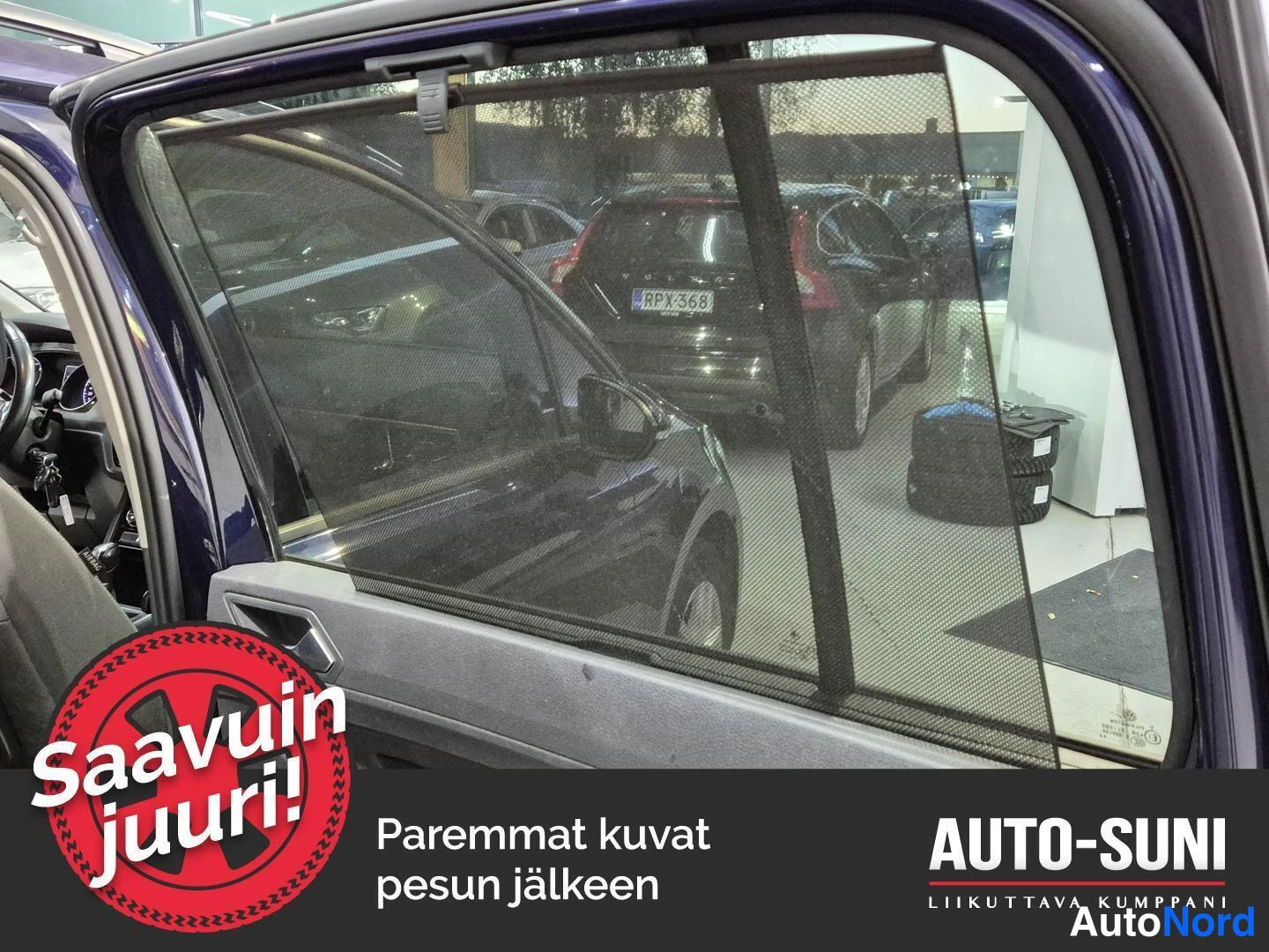 Yksityiskohta: Ava­tu­n ta­kan­oi­vin ik­ku­naan kiin­ni­lii­ty­ne­ä au­rik­kon­ver­ho ja taa­kse­nä­ky­vät au­tot huo­ne­os­te­ron sisällä.
