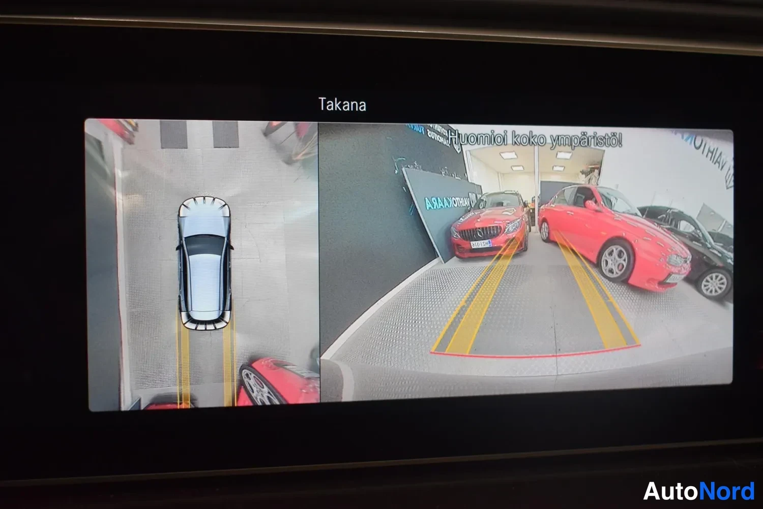 Yksityiskohta: Näytöllä peruutuskamera ja 360-kaistanäkymä; otsikossa 'Takana' ja varoitus 'Huomioi koko ympäristö!'.